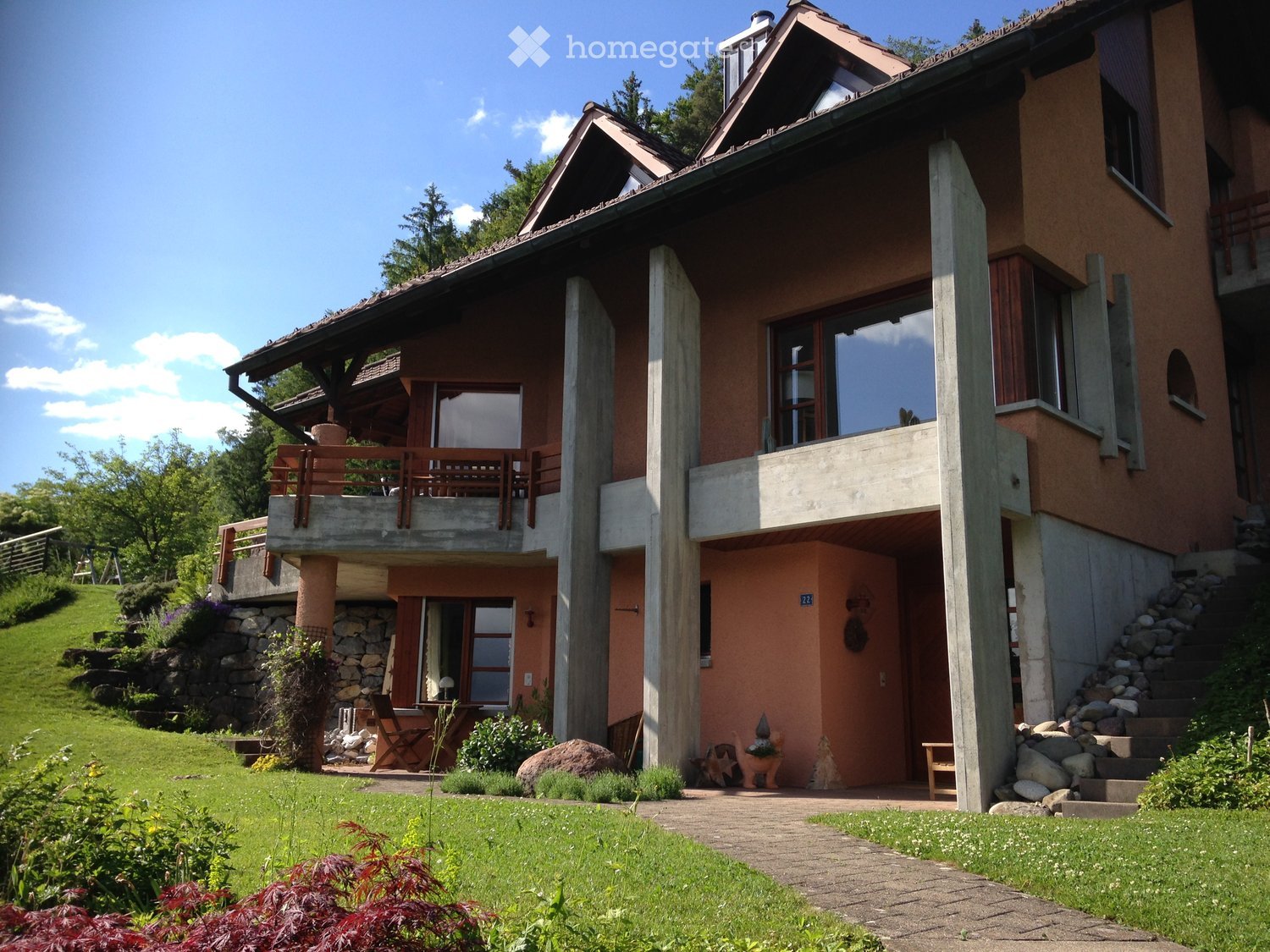 2 story house, brown exterior, large windows, balcony, concrete pillars, garden, stone steps