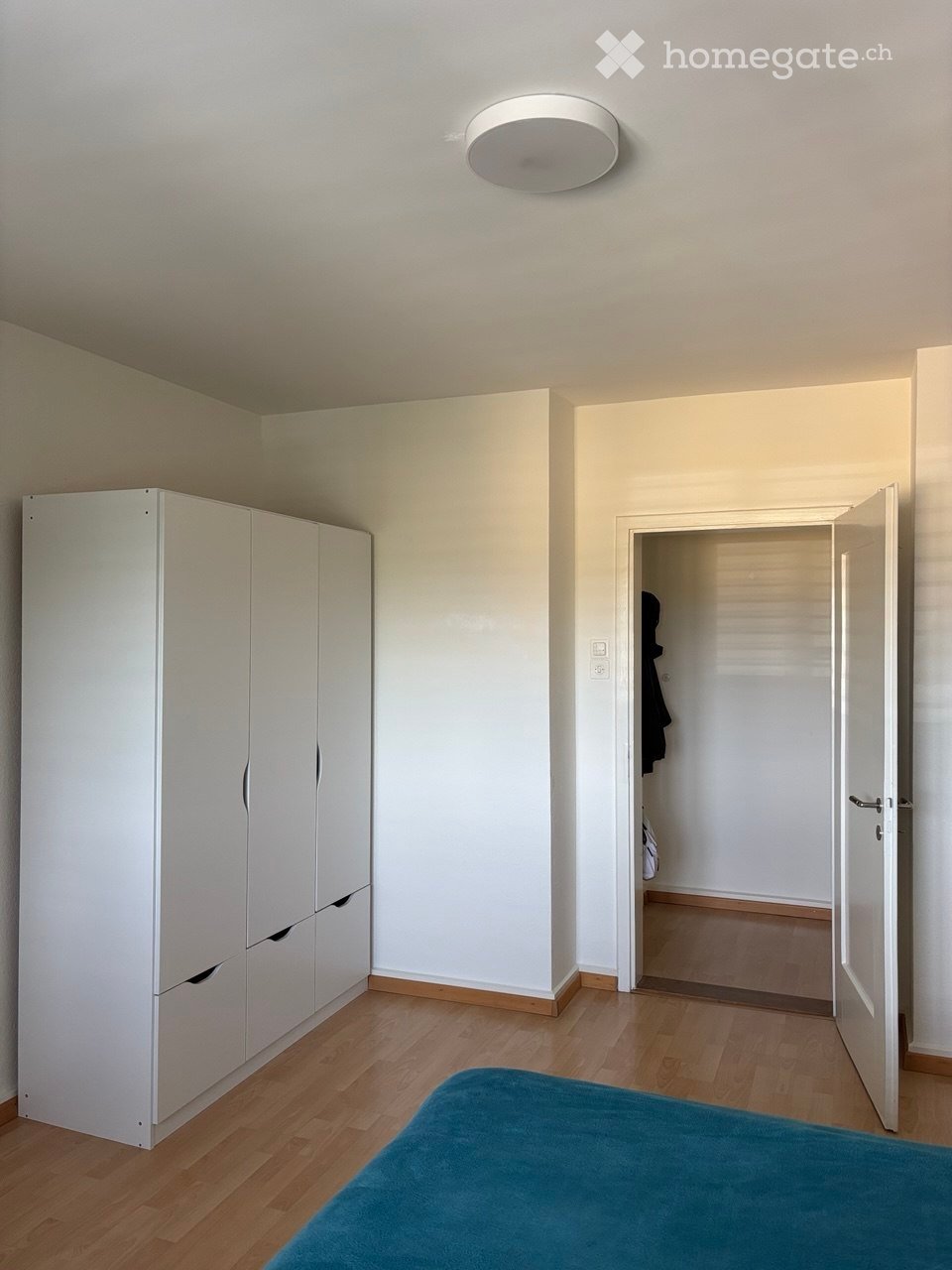 A modern, minimalistic bedroom with a blue bedspread, white wardrobe, and wooden flooring.