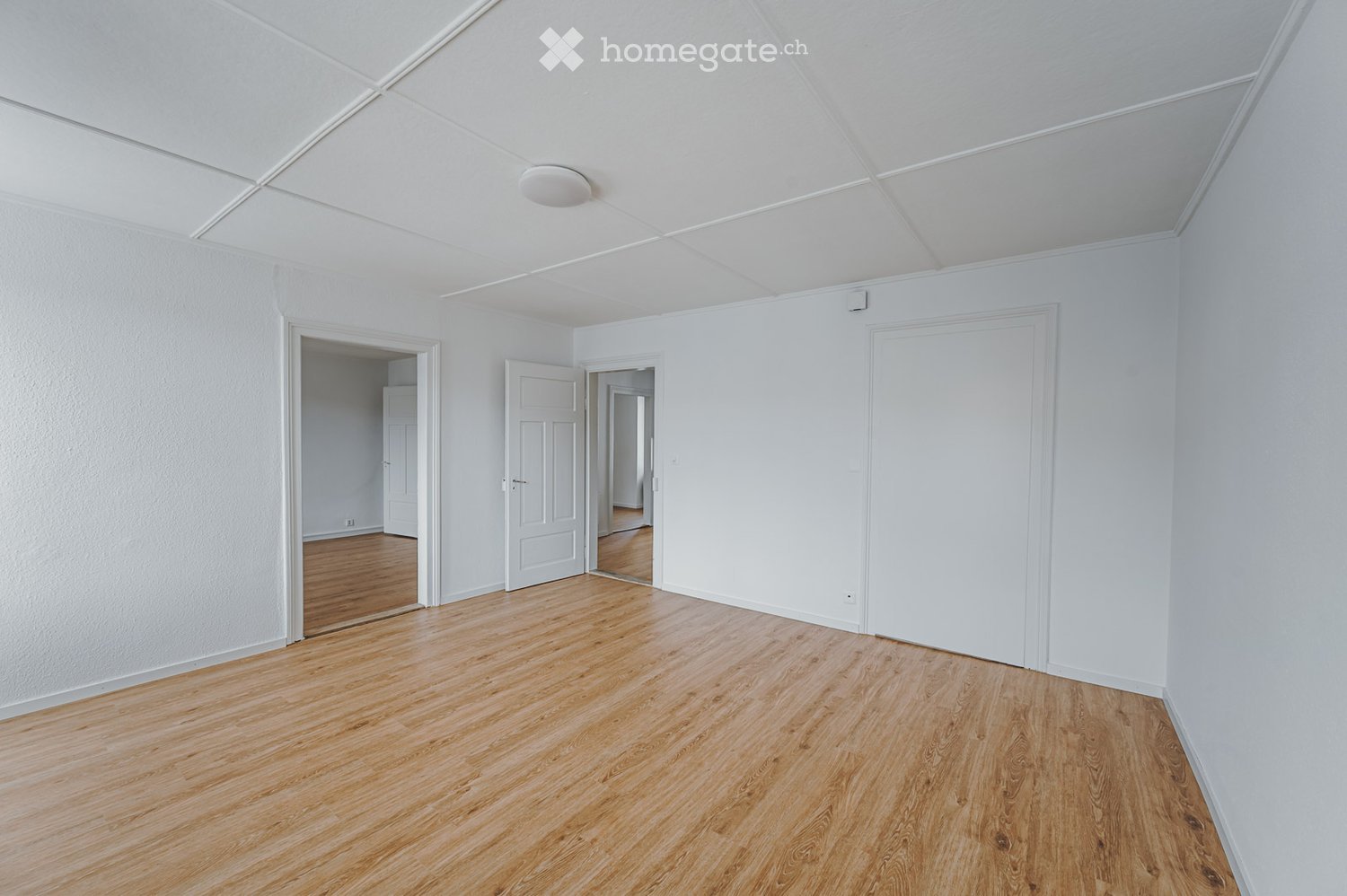 Unfurnished Room. Completely empty room with white walls, wooden floor, and three doors leading to other rooms.