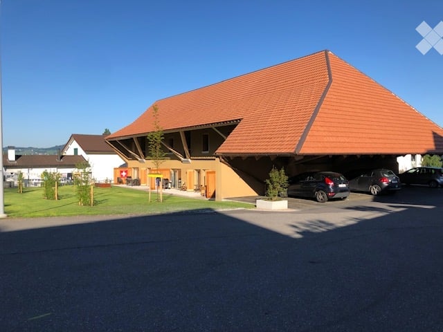 Modern architectural design with a large red roof and yellow walls, several cars parked in the carport.