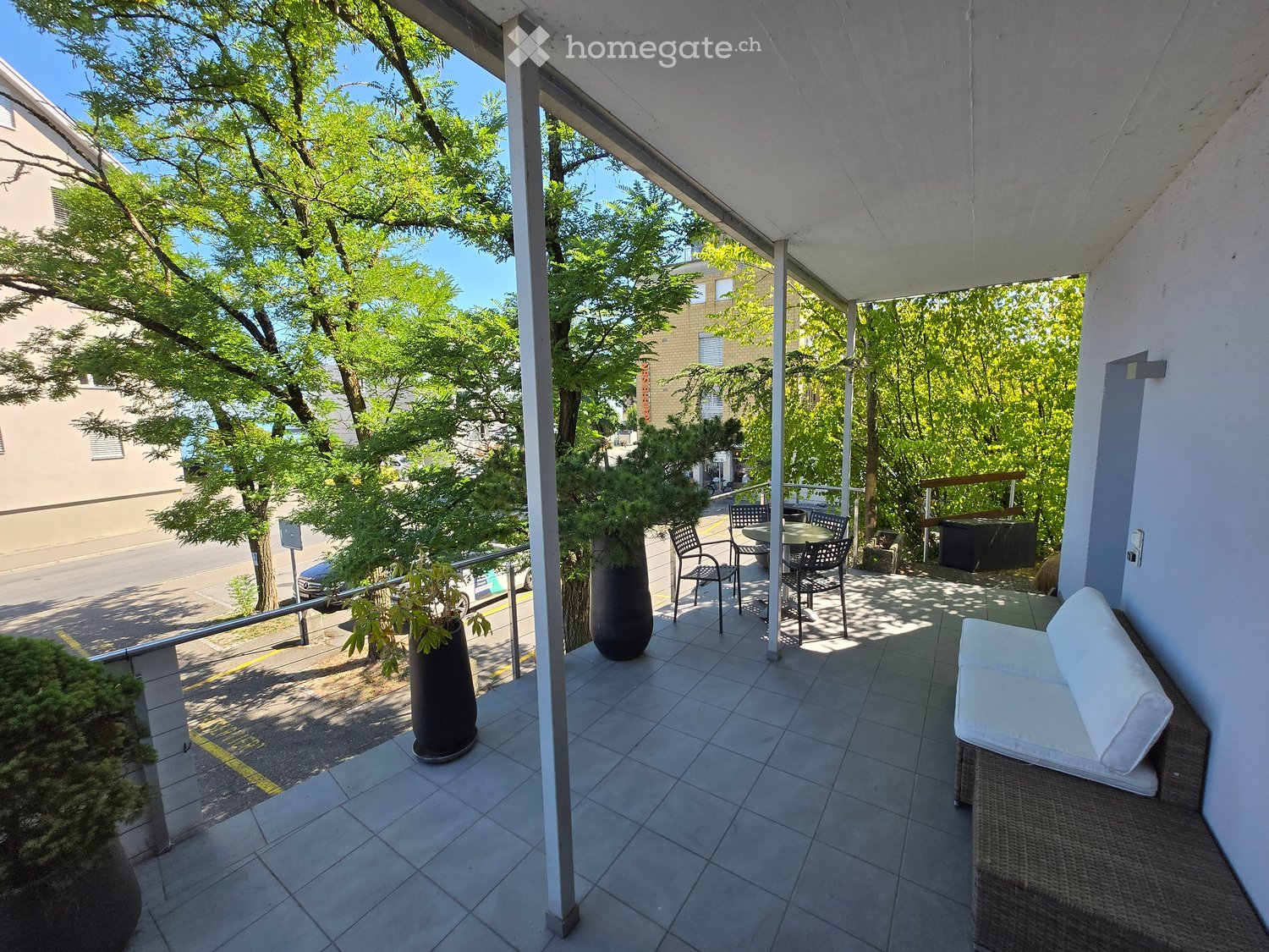 Balcony with tiled floor, white sofa, small table and chairs, and potted plants.