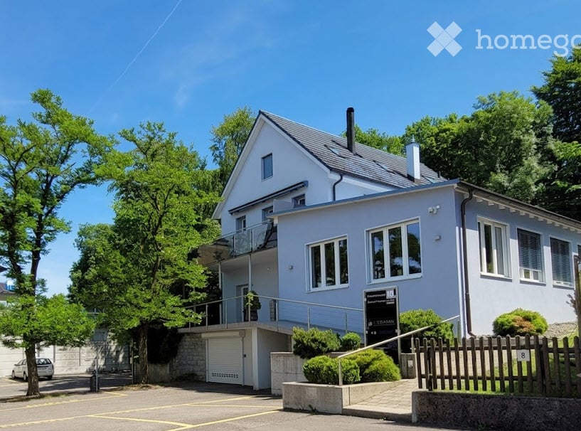 Two-story house with light blue exterior, white trim, garage, balcony, and well-maintained garden.