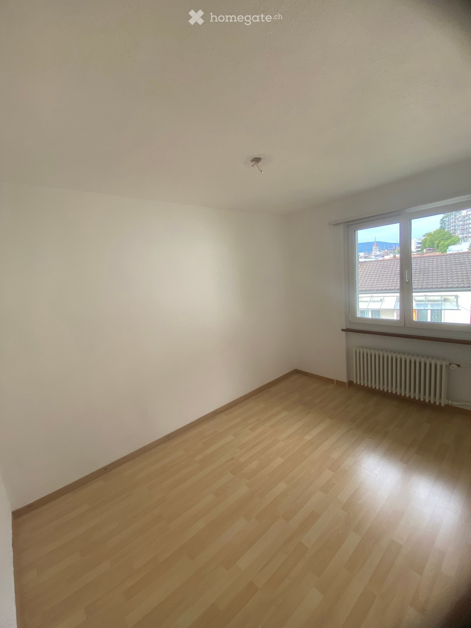 Empty room with wooden flooring, white walls, and a window with a radiator below it.