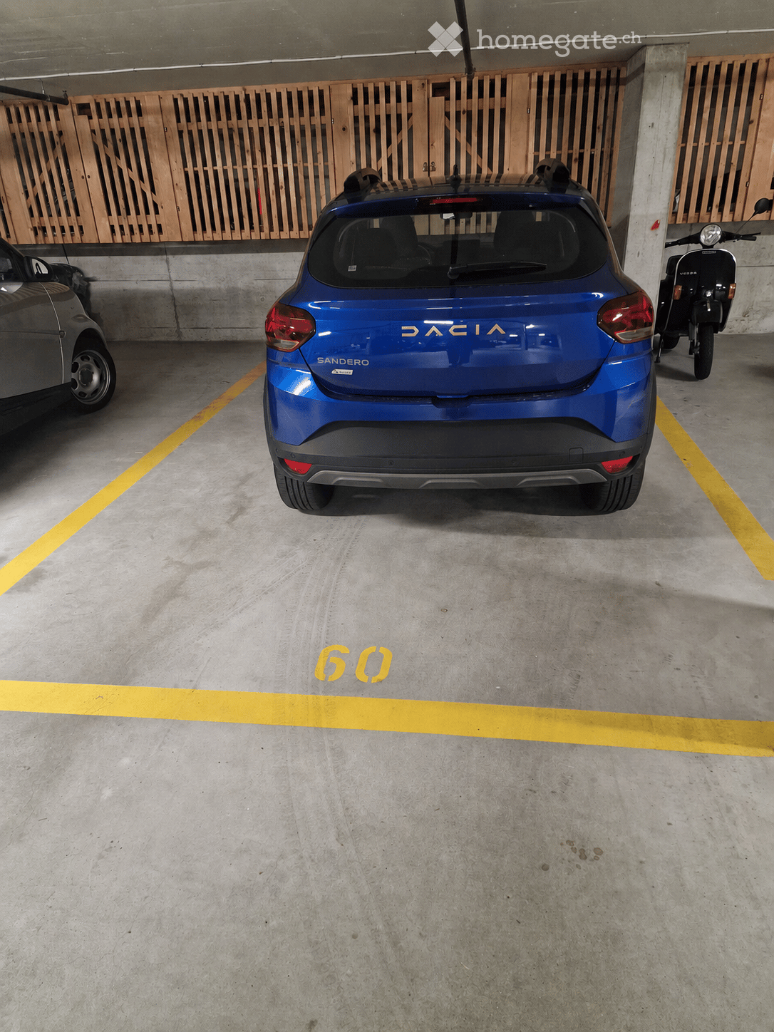 Underground parking area with a blue Dacia Sandero car, a scooter, and a grey car parked in designated spots.