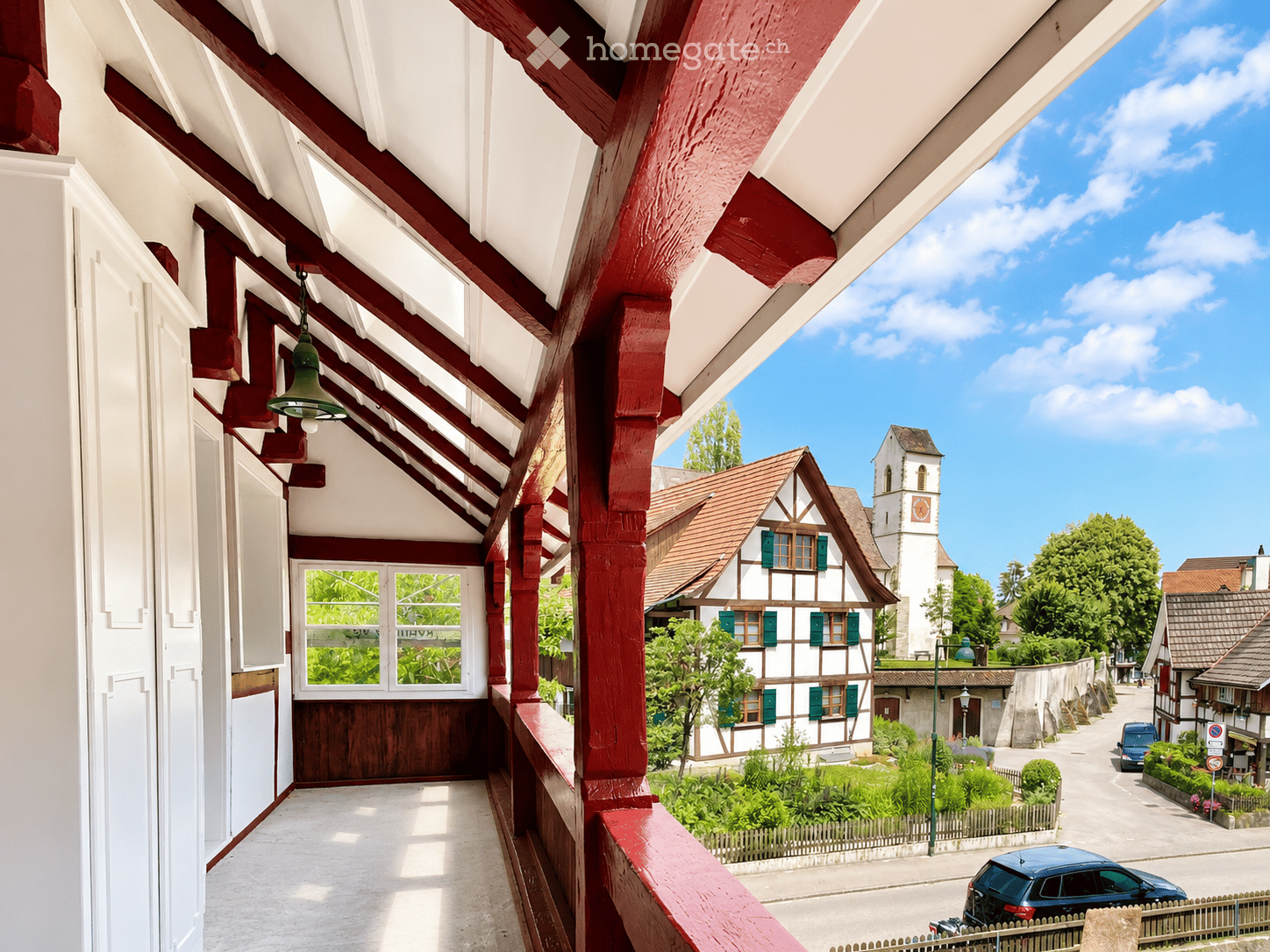 Balcony overlooking a picturesque village with traditional houses, a church tower, and a clear blue sky.