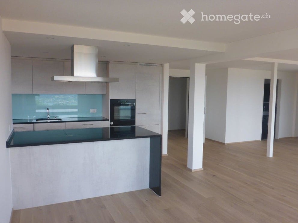 Modern kitchen with a central island, sleek cabinets, a stainless steel range hood, and a black countertop.