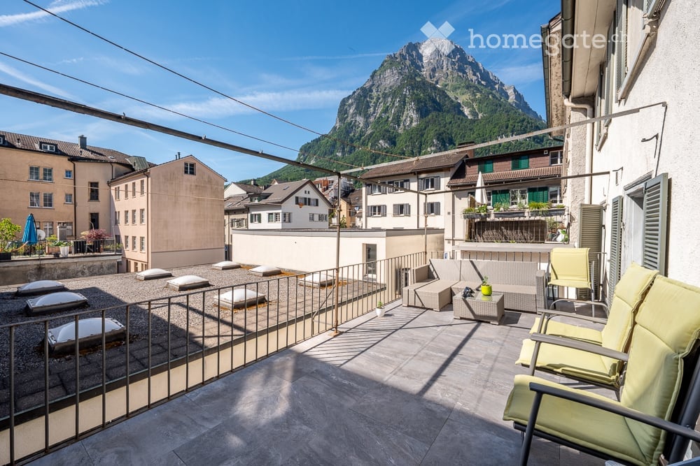 Balcony with a view of a mountain, featuring a sofa, a small table, and a couple of chairs.