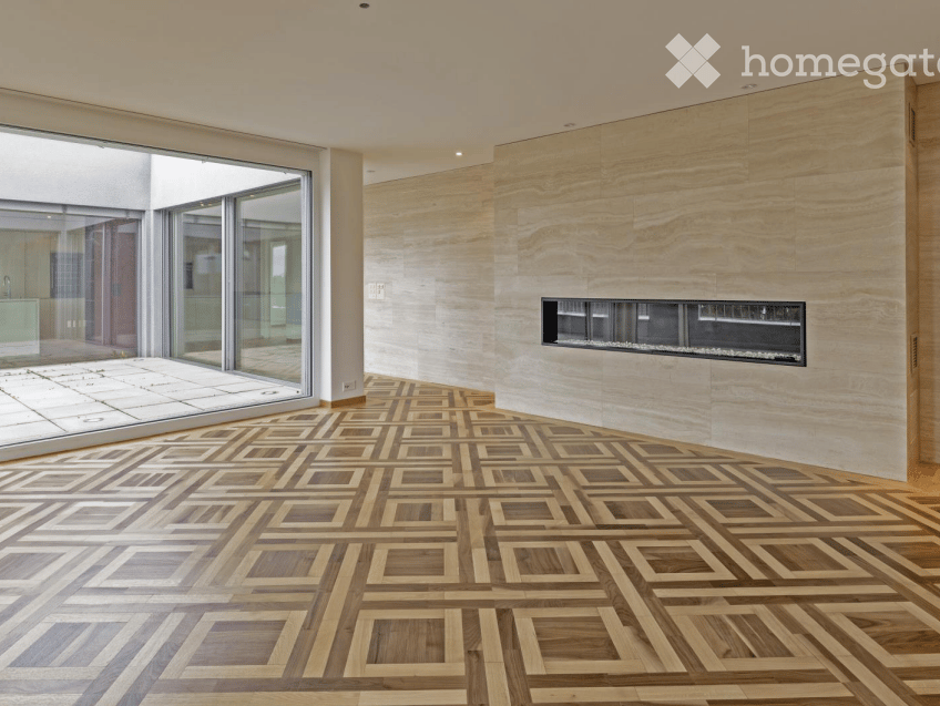 Modern unfurnished room with a geometric wooden floor, large glass sliding doors, and a built-in fireplace.
