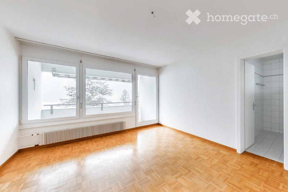 Empty room with wooden flooring, large windows, radiator, and a view of a balcony area.