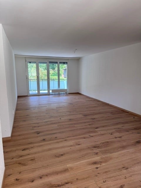 Empty room with wooden flooring, white walls, and large glass doors leading to a balcony.