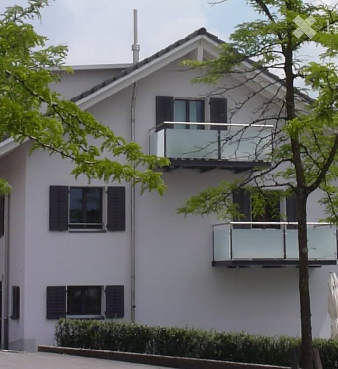Modern two-story house with white exterior, black shutters, and two balconies with glass railings.