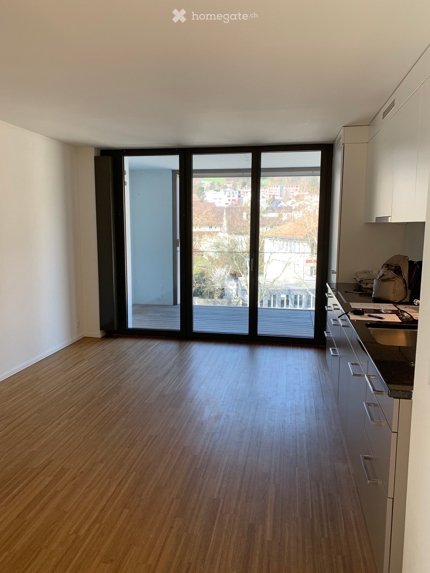 Empty room with wooden flooring, white walls, and large sliding glass doors leading to a balcony with a city view.