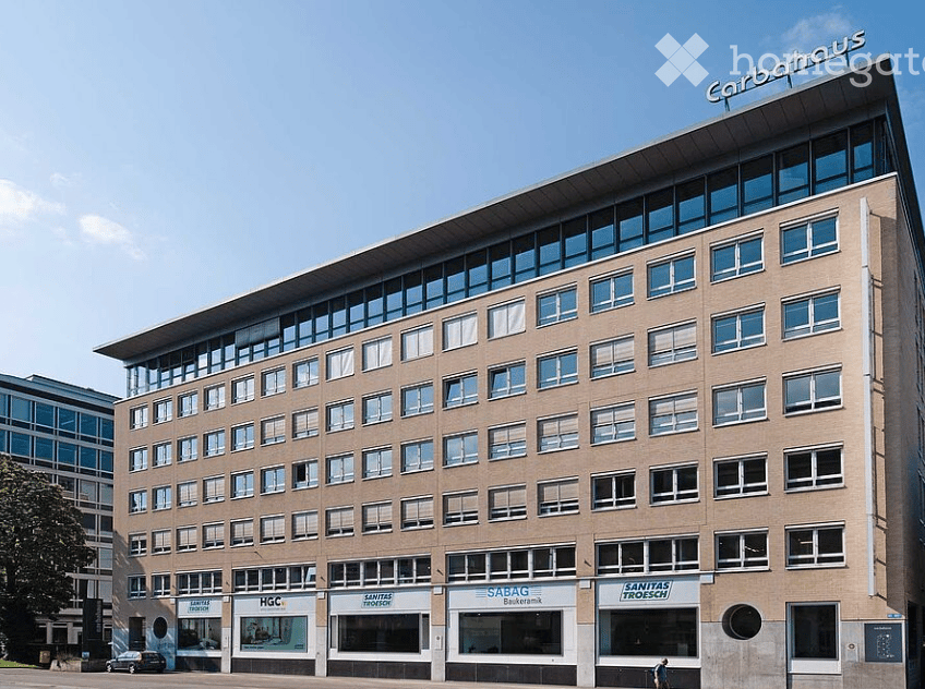 Modern multi-story building with a flat roof and large windows, featuring commercial signage for 'Carbahaus' and other businesses.