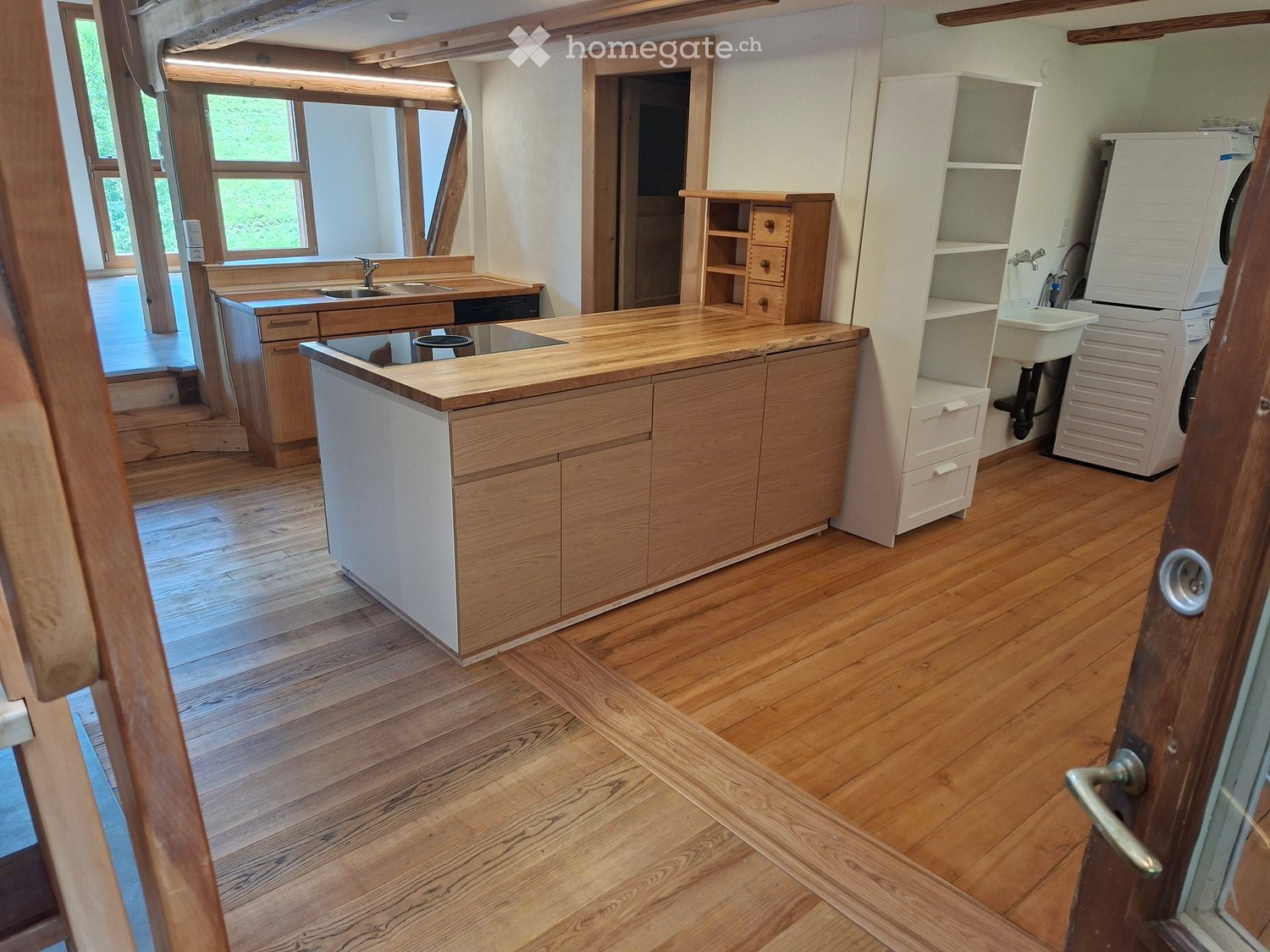 Well-lit kitchen with wooden floors, a central island, sink, and cabinetry. Includes a washing machine and dishwasher.