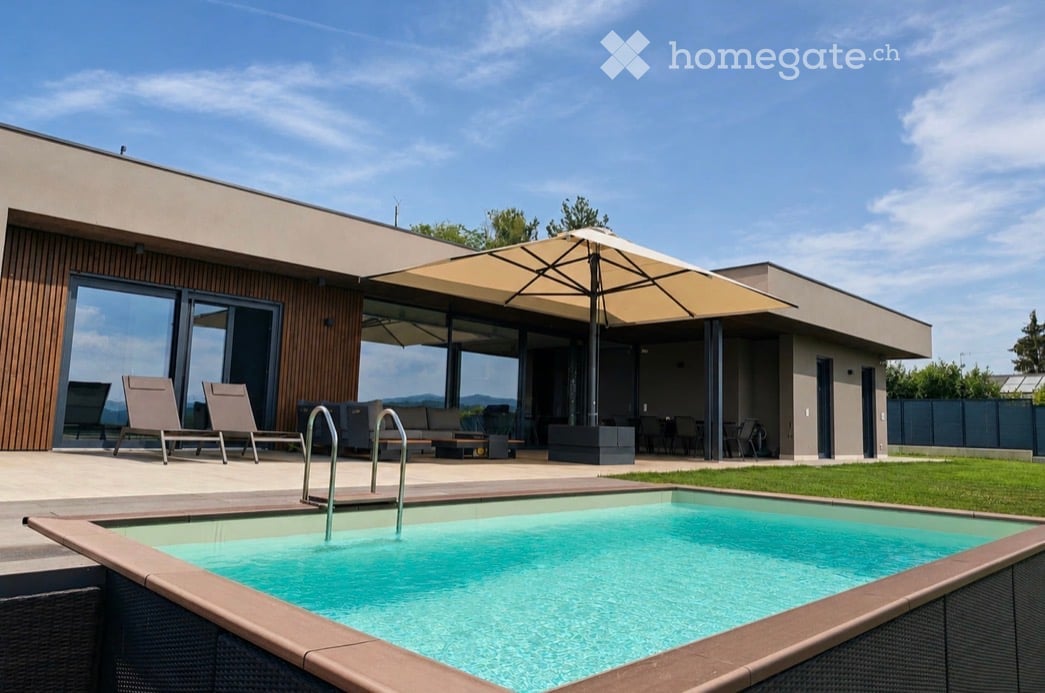 Modern outdoor area with a swimming pool, lounge chairs, umbrella, and patio furniture near a contemporary house.