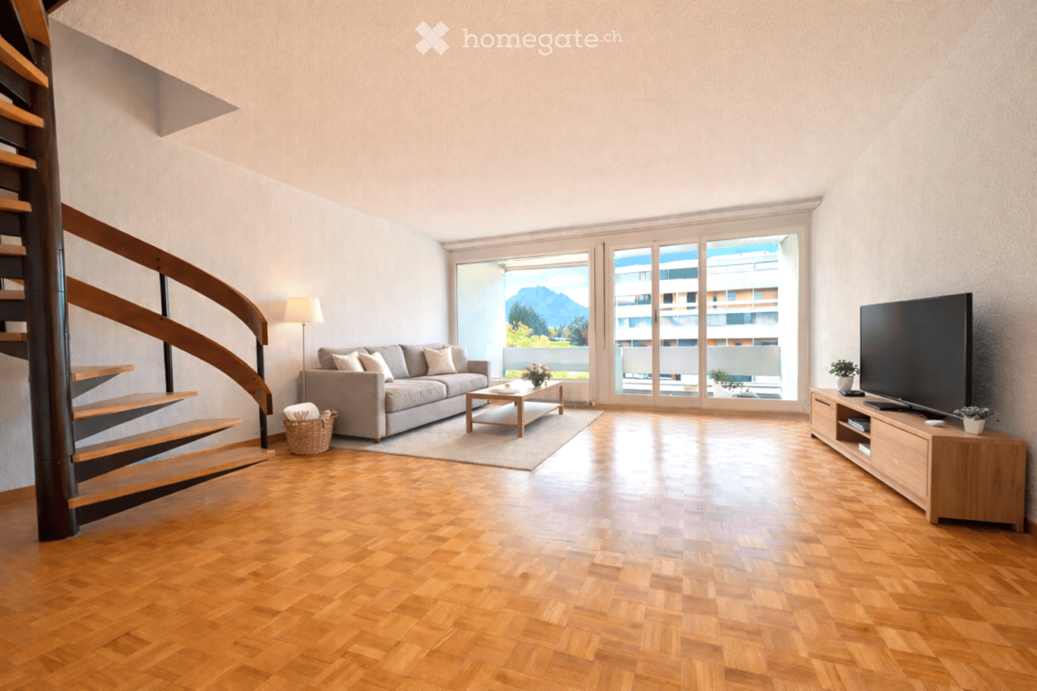 wooden floor, gray couch, coffee table, TV, lamp, spiral staircase, large windows