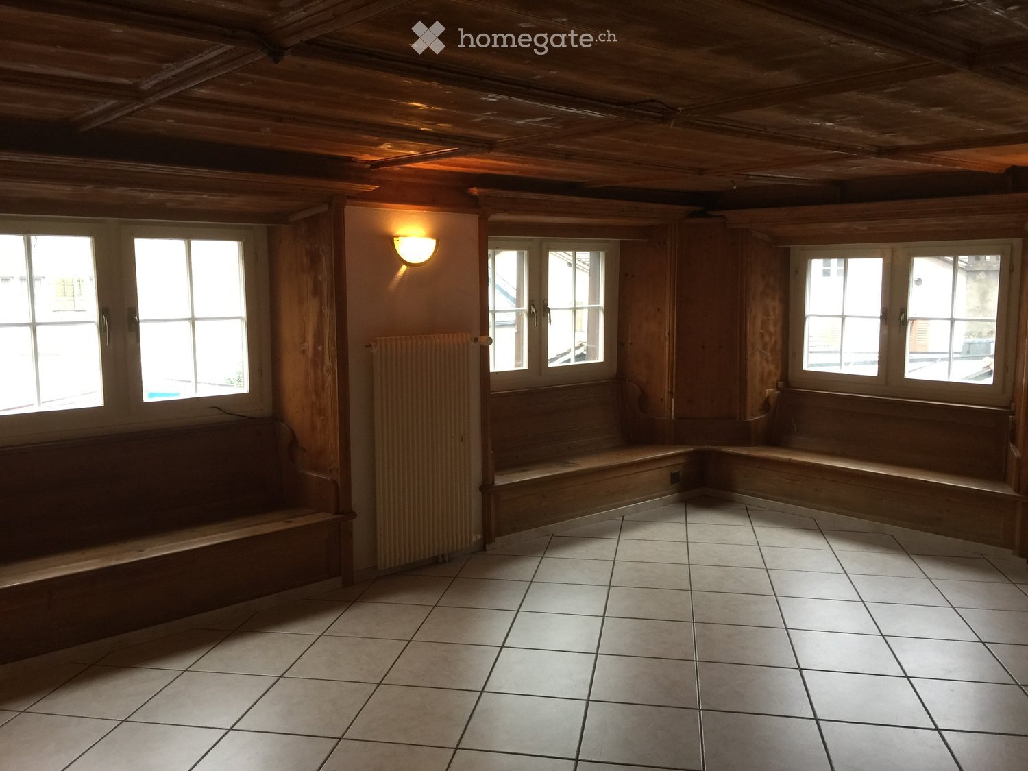 Empty room with wooden walls, tiled floor, built-in wooden benches, and large windows letting in natural light.