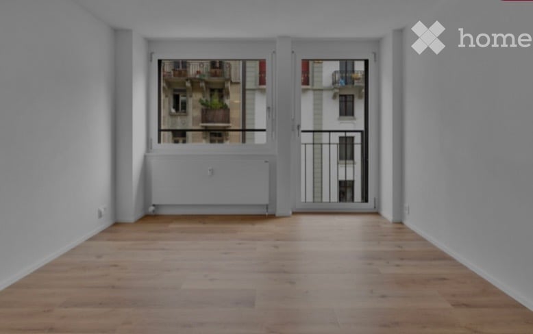 Empty room with wooden flooring, large window with balcony access, radiator, and white walls.
