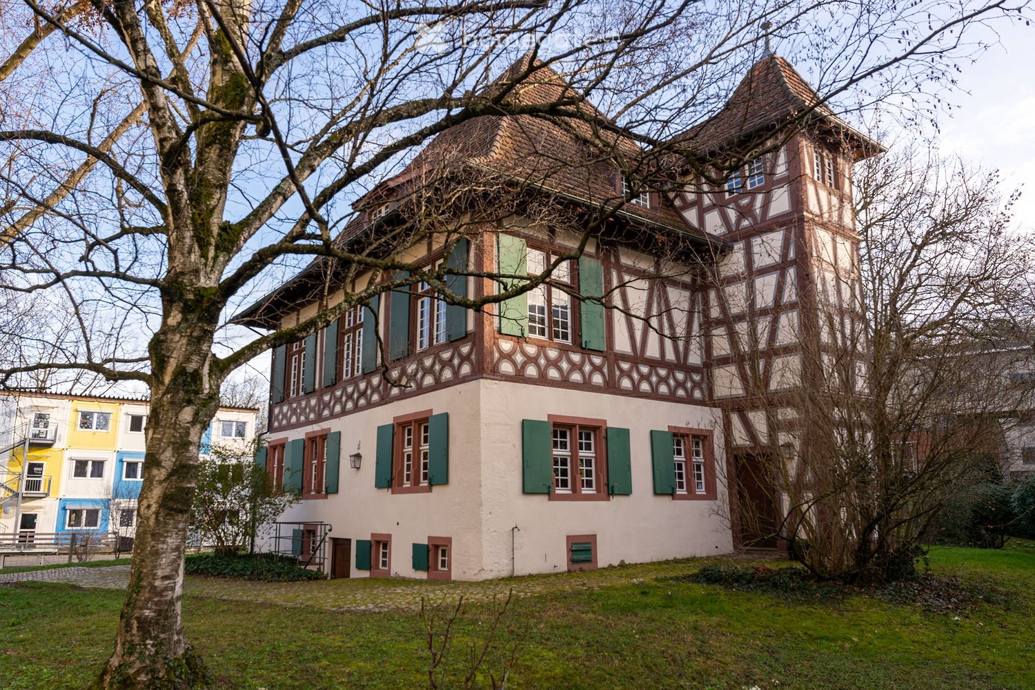old traditional style, white and brown walls, green shutters, trees around, yard, several windows