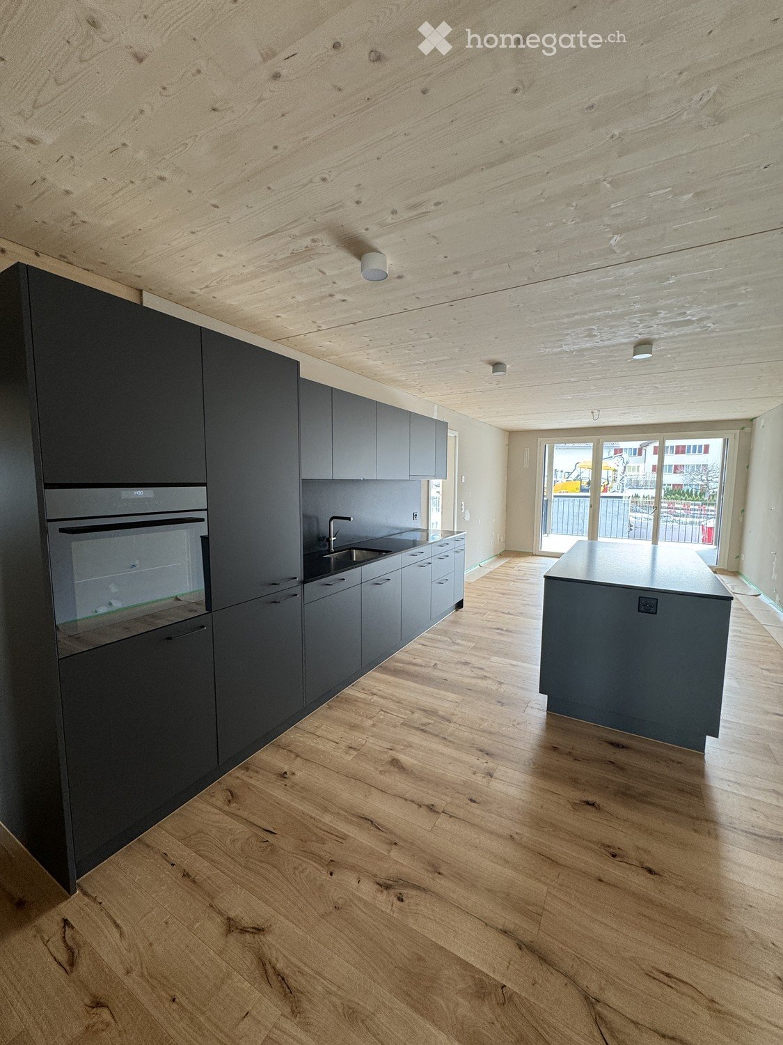 Modern kitchen with dark grey cabinets, wooden flooring, and a central island. Features an oven, sink, and faucet.
