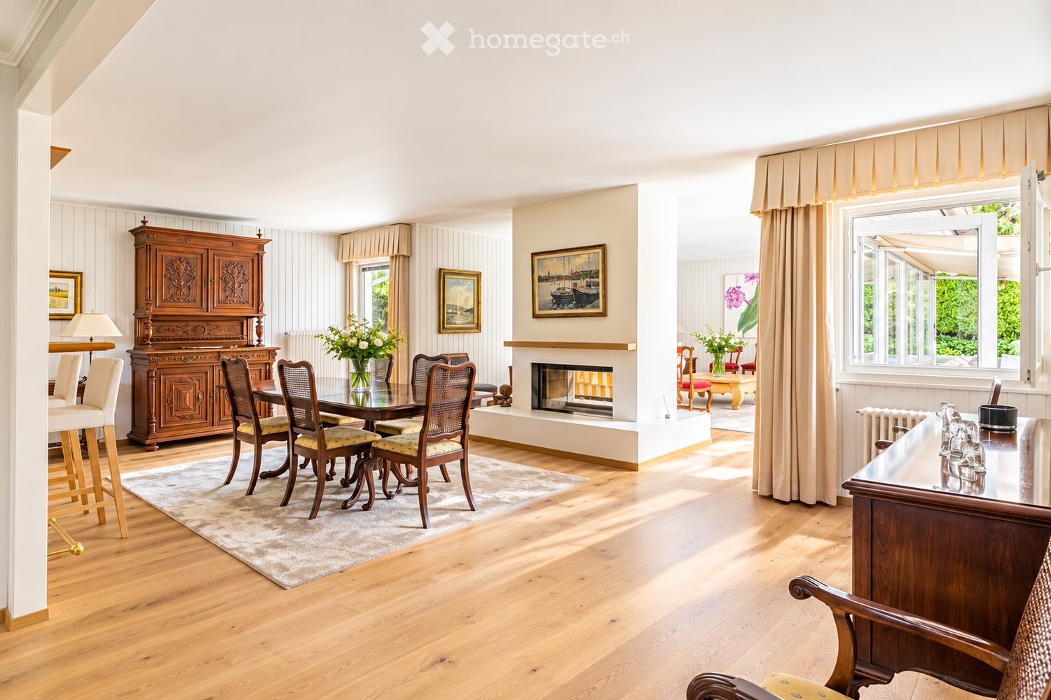 Elegant dining area with wooden flooring, a fireplace, a large dining table with chairs, a wooden cabinet, and decorative vases.