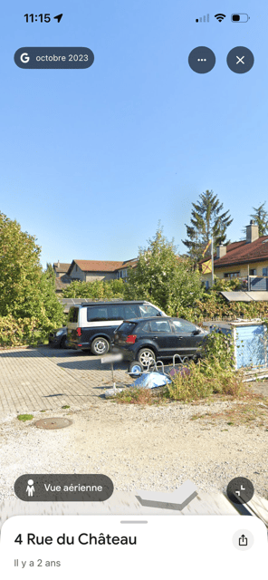 Outdoor parking area with several parked cars, surrounded by greenery and trees, with a clear blue sky above.