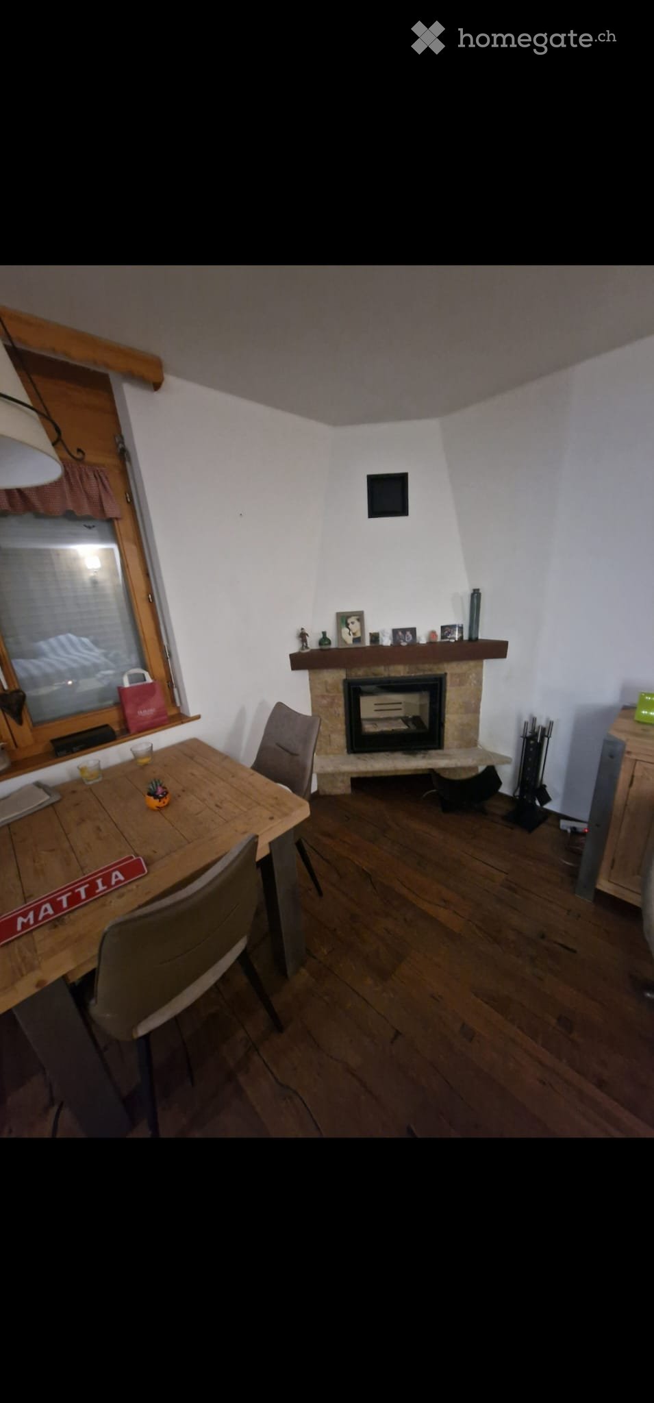 Cozy living room with wooden floor, fireplace, dining table, chairs, and decorative items on the mantel.