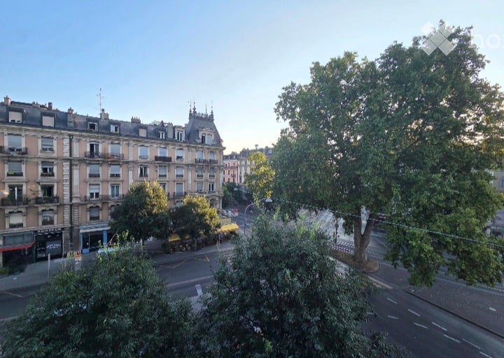 Balcony overlooking a city street with classic European buildings, trees, and a clear sky.