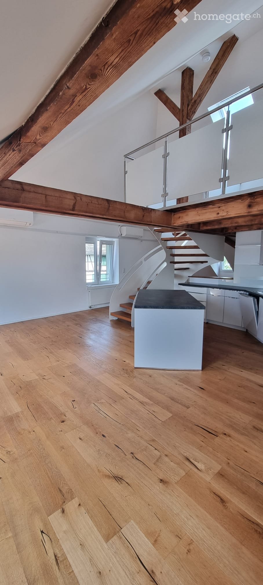 Open, airy hallway with wooden floors, exposed wooden beams, and a modern staircase with glass railing leading to an upper level.