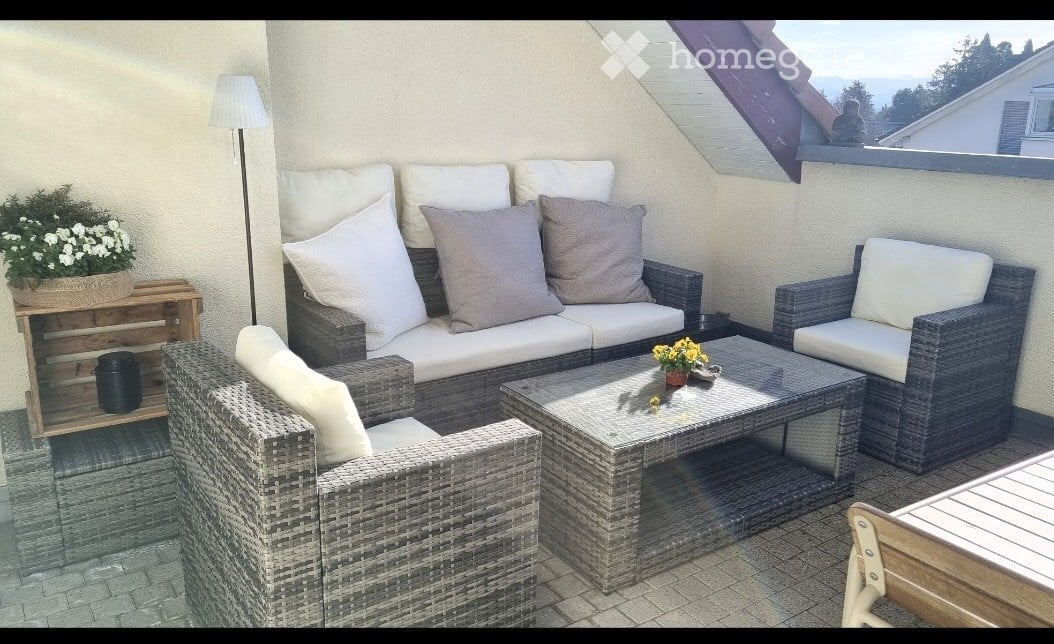 A modern outdoor seating area with wicker furniture, including a sofa, armchairs, and a coffee table, set against a backdrop of a scenic view.