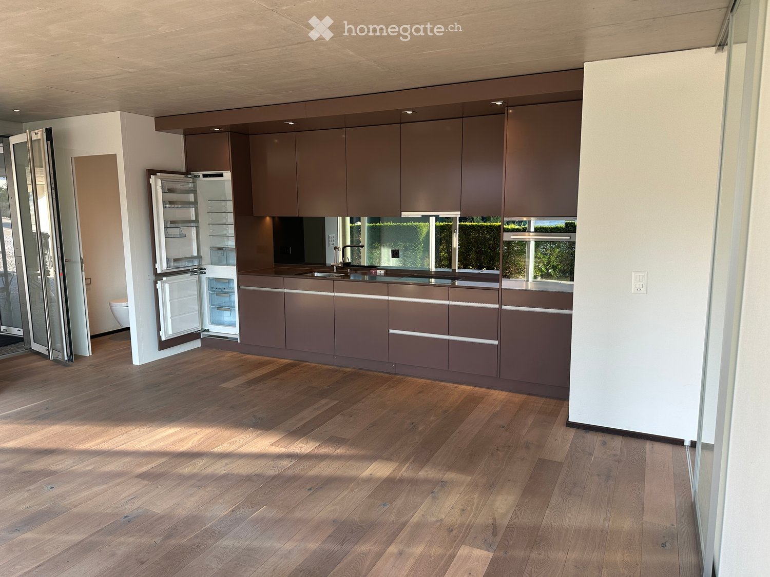 Modern kitchen with wooden flooring, dark brown cabinets, and a stainless steel refrigerator. The sink area features a modern faucet and ample counter space.