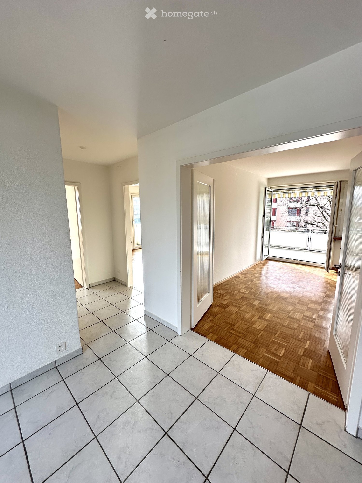 empty room with two doors, balcony, wooden flooring at one end, white tiling