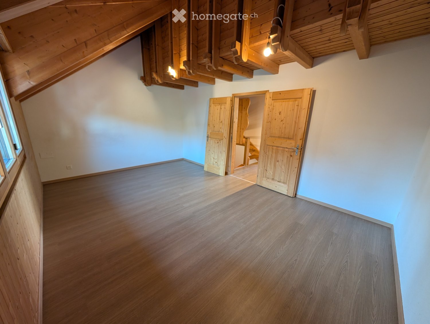 Empty room with wooden flooring, exposed wooden beams on the ceiling, and a doorway leading to another space.