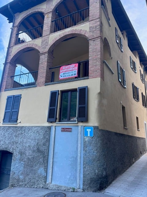 Multi-story building with arched balconies, shutters, and a sign advertising apartments for rent.