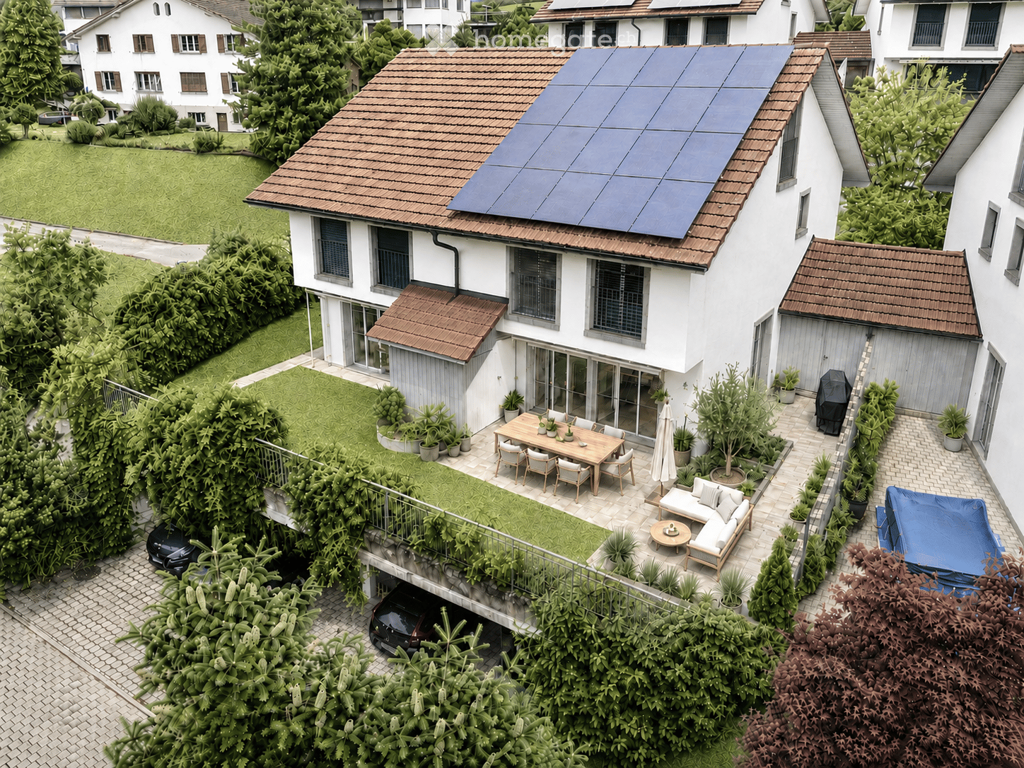 A modern two-story house with a solar panel roof, surrounded by greenery and a well-maintained garden. The house features a spacious patio with outdoor furniture, including a dining table, chairs, a sofa, and a coffee table. There is also a covered parkin