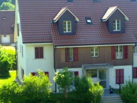 Two-story residential house with a red-tiled roof, multiple dormer windows, and a well-maintained garden in front.