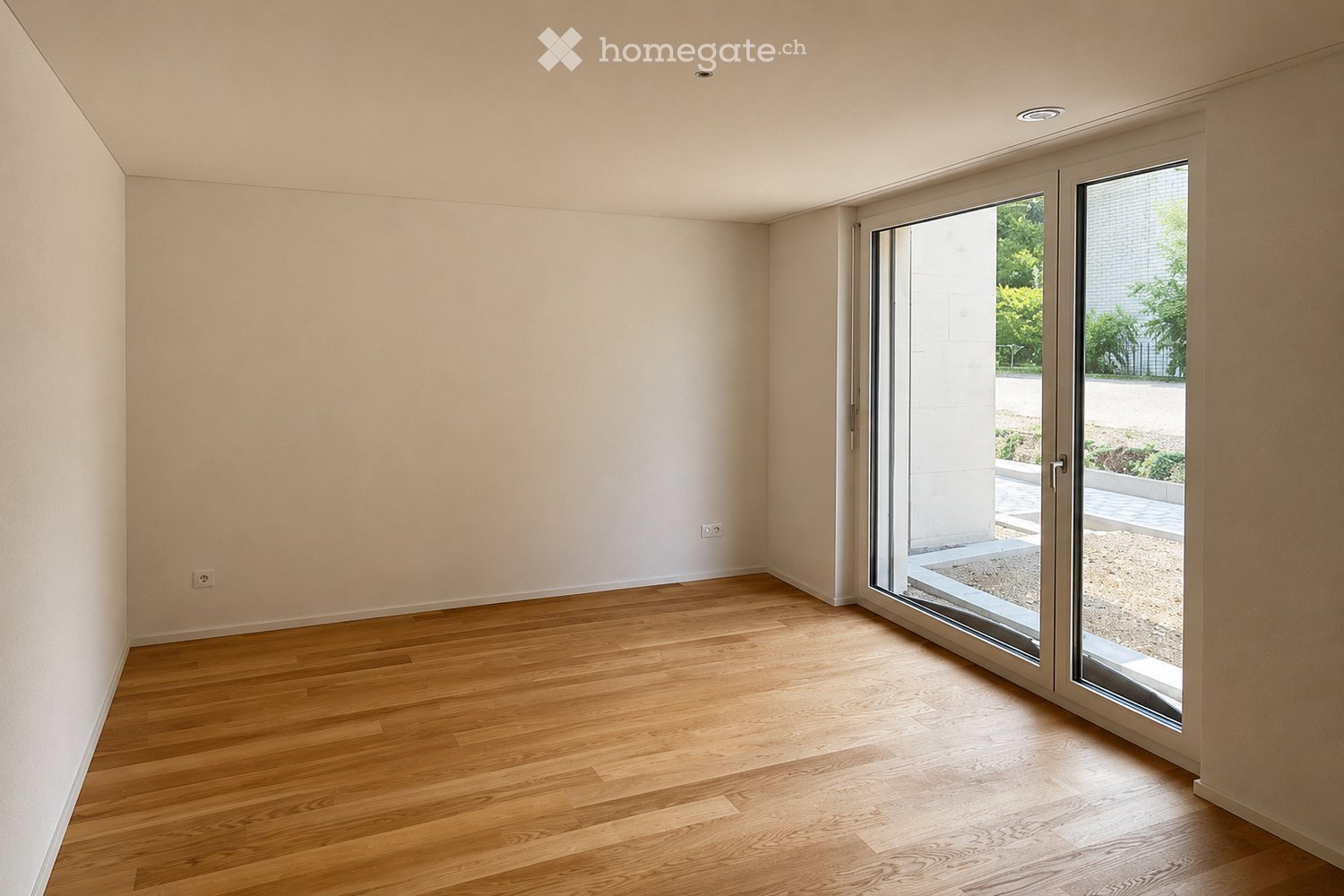 Empty room with light-colored walls and wooden flooring, featuring large sliding glass doors leading to an outdoor area.