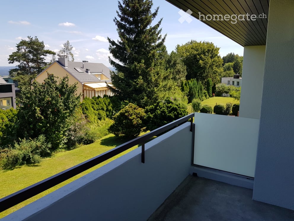 Balcony with a view of a green garden, trees, and neighboring houses.