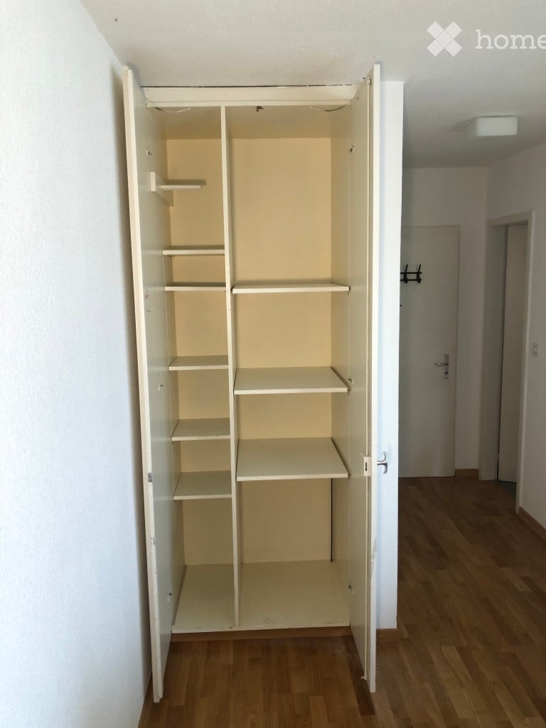 Empty room with wooden flooring and a large open wardrobe with multiple shelves.