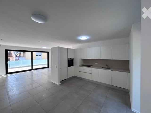 Modern kitchen with white cabinets, grey tiles, and a large window opening to a balcony.