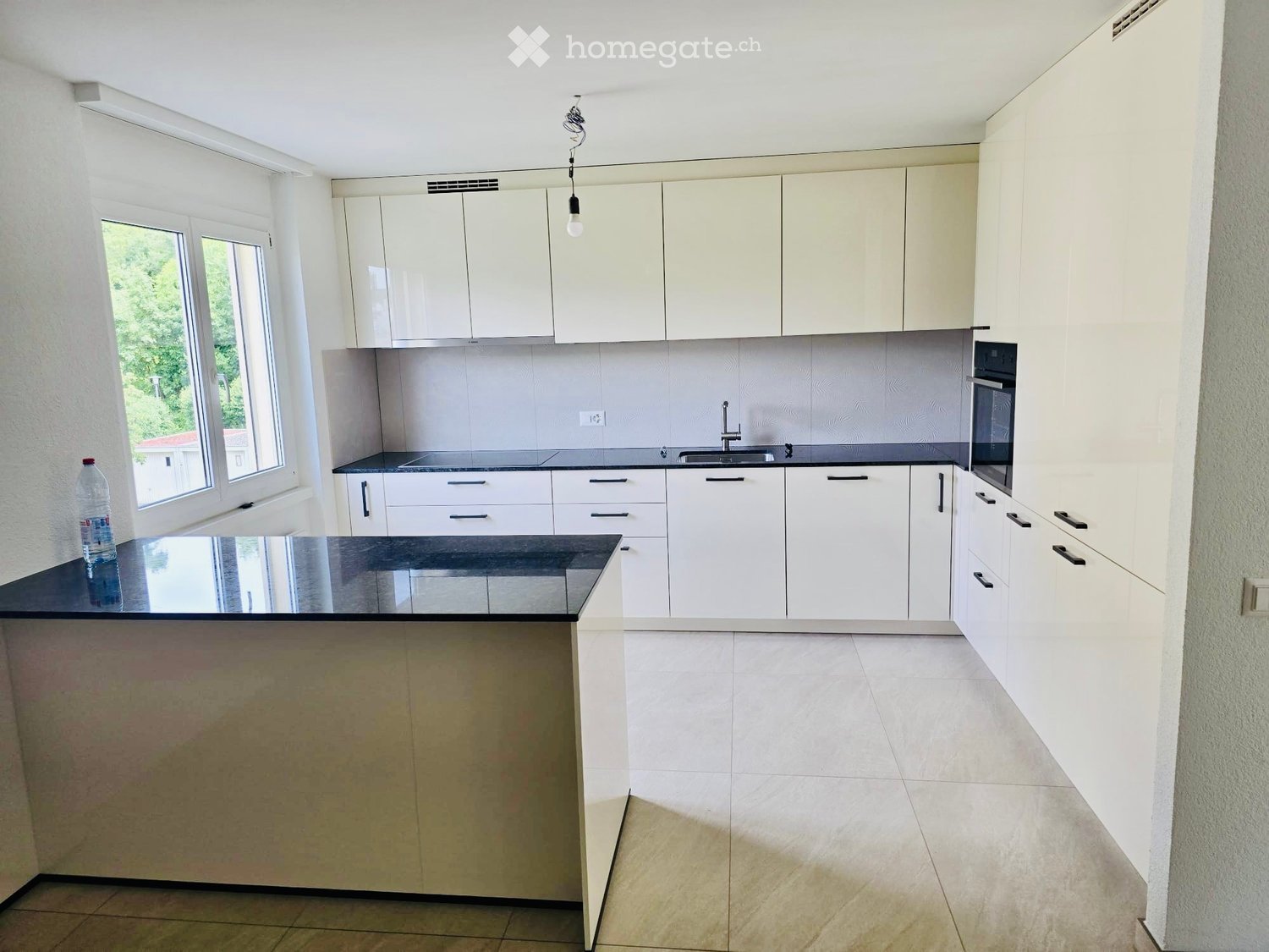 Modern kitchen with white cabinets, black countertops, and a central island. Features include a sink, oven, and a bottle on the island.