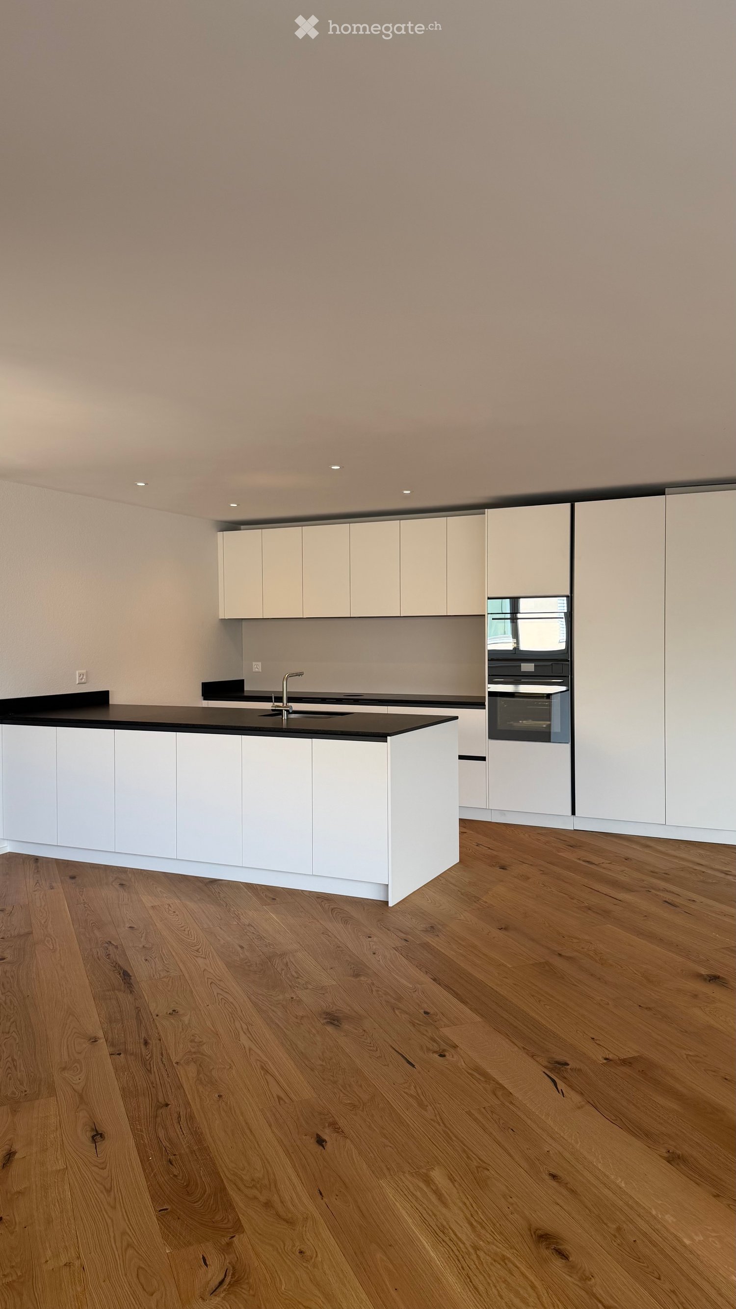 Modern kitchen with white cabinets, black countertop, and wooden flooring.