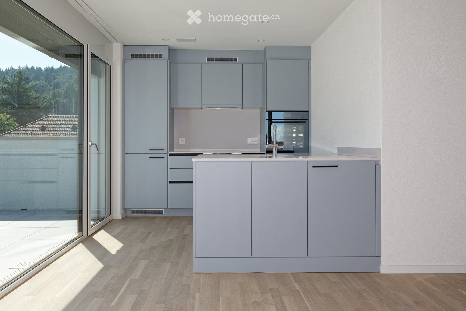 Modern kitchen with grey cabinets, a central island, and a large window offering a view of the outdoors.