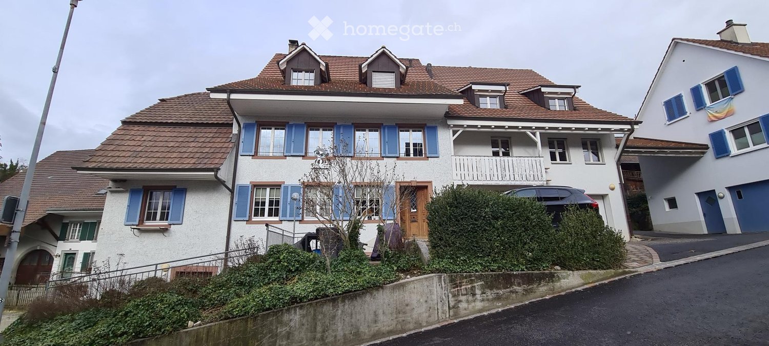 3 story house, white walls, brown roof, multiple windows with blue shutters, balcony, car parked outside