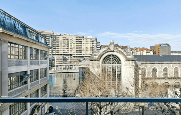 Balcony overlooking a cityscape with modern and historic buildings, a canal, and a clear blue sky.