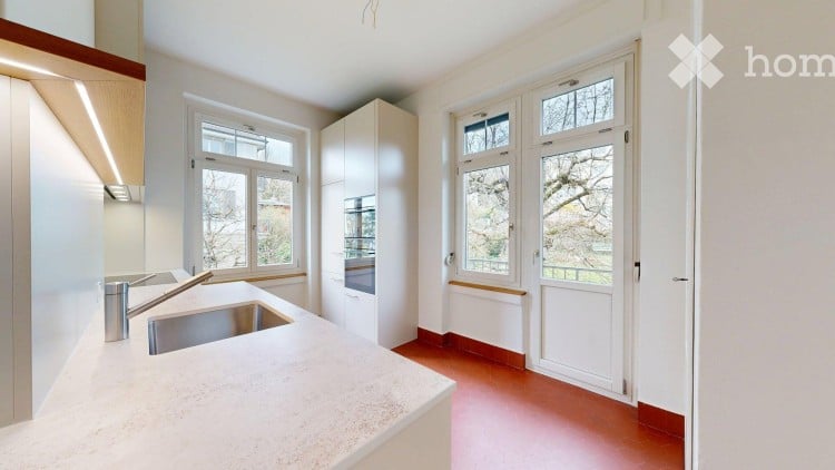Modern kitchen with white cabinets, a stainless steel sink, and a granite countertop. The room features large windows and red flooring.