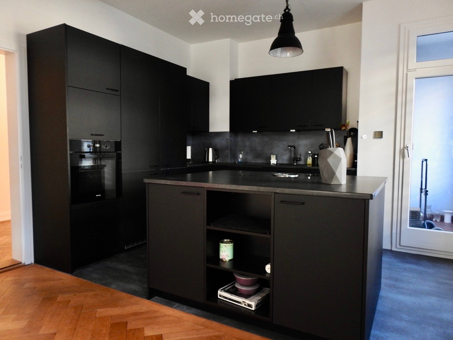 Modern kitchen with black cabinets, stainless steel appliances, and a central island with open shelving. Includes a sink, faucet, and decorative vase on the counter.