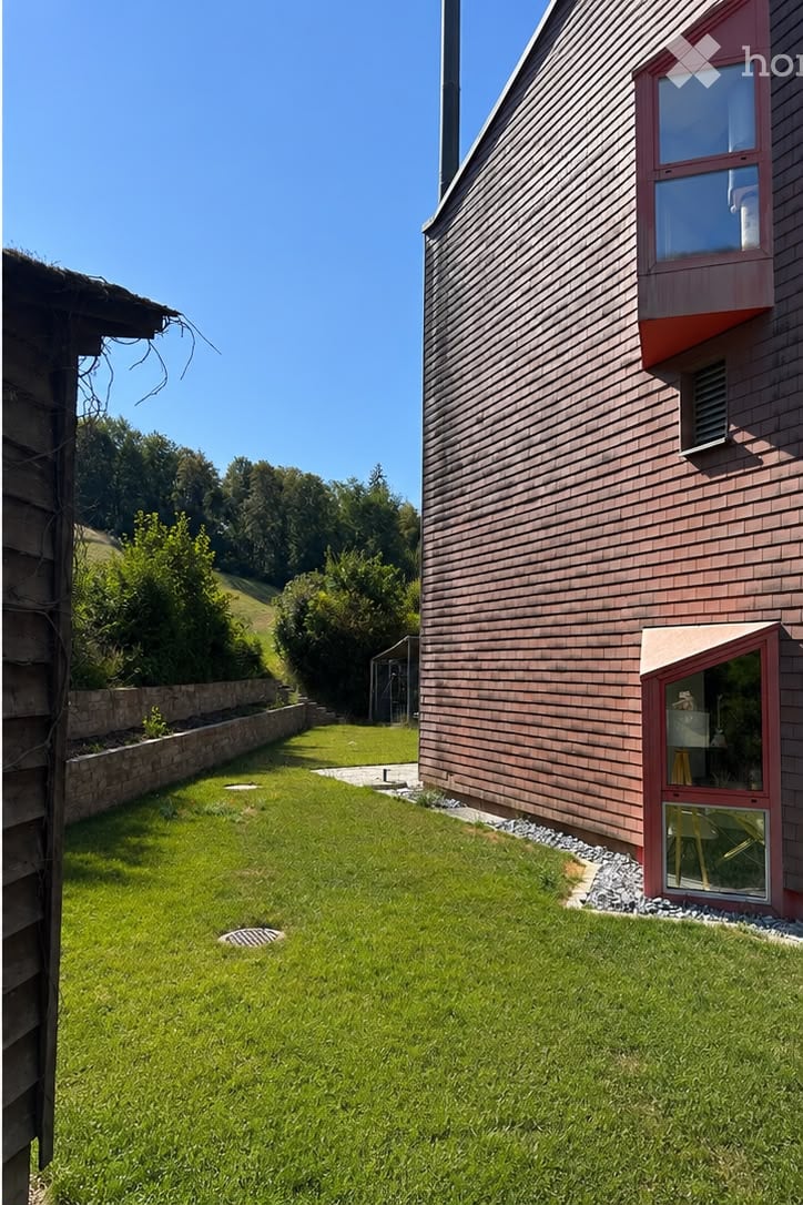 Well-maintained lawn with a stone border, a wooden house with a red-framed window and door, and a clear blue sky in the background.