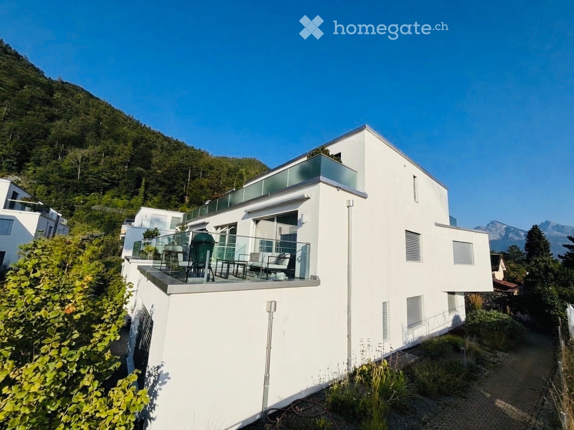 Modern white house with large glass balcony overlooking a scenic mountain view.