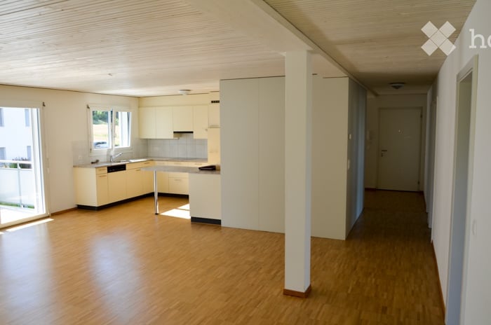 Bright, modern kitchen with light-colored cabinets, a central island, and wooden flooring. The space is open and well-lit with large windows.